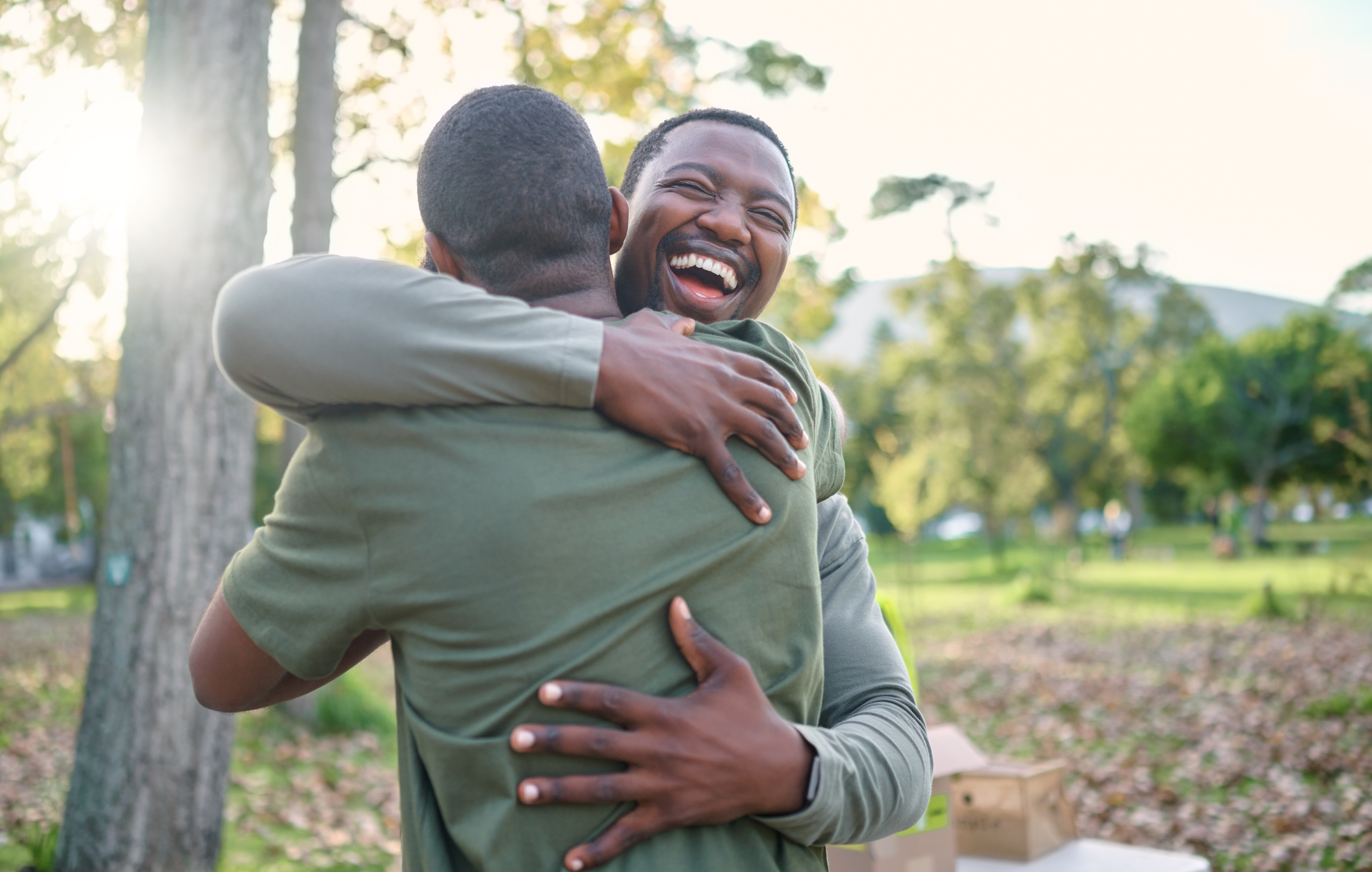 Charity, happy and hug with volunteer friends in a park for community, charity or donation of time together. Support, teamwork or sustainability with a black man and friend hugging outdoor in nature.